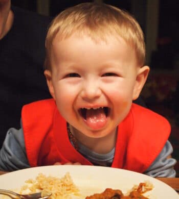 Kleinkind streckt über einem Teller mit Essen die Zunge heraus