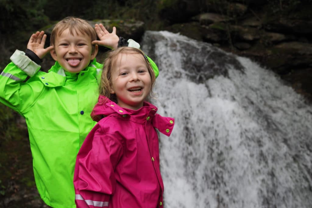 Kinder in Regenkleidung vor Wasserfall