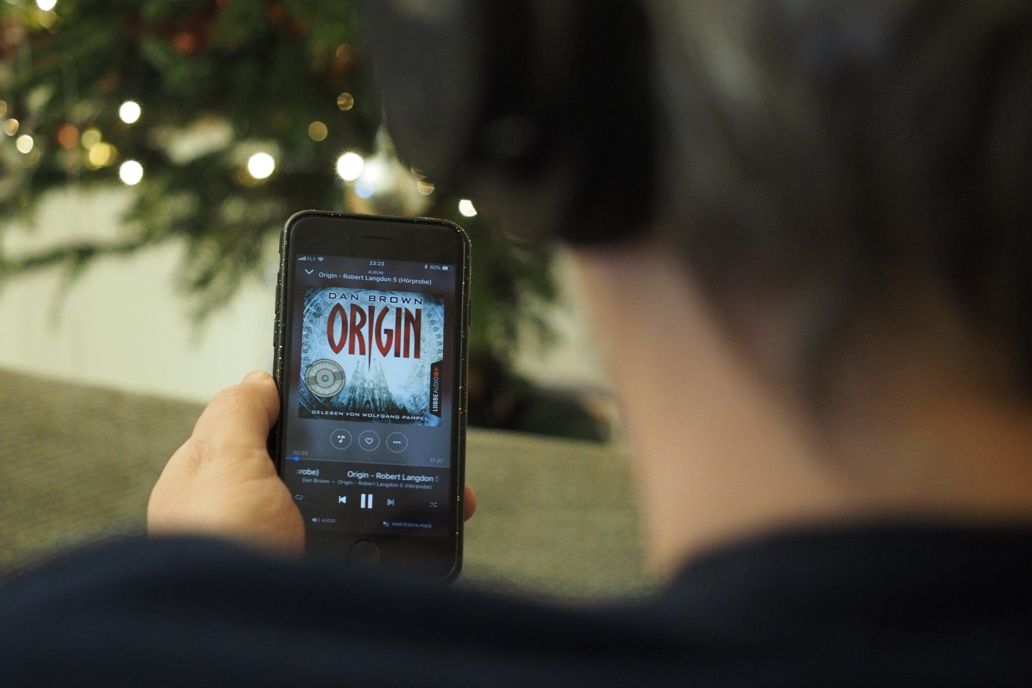 Mann mit Kopfhörern sieht sich das Cover des Hörbuchs Origin von Dan Brown am Smartphone an