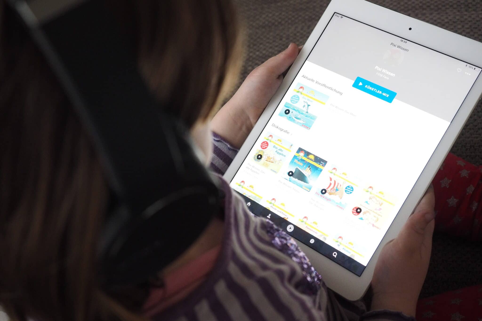 Deezer, Kind mit Kopfhörern schaut sich Hörbücher am iPad an