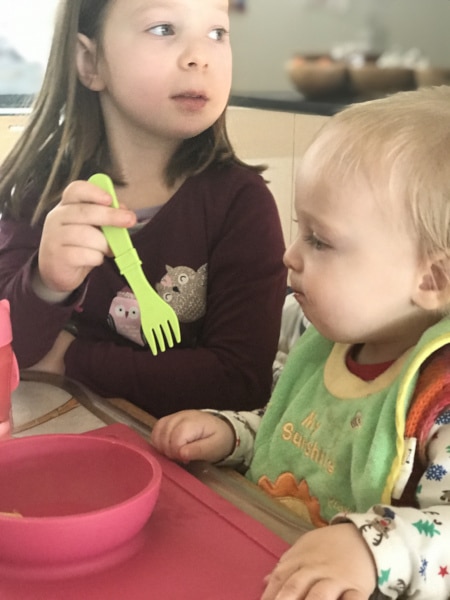 Mittagstisch Mädchen füttert mit Gabel ihre kleine Schwester