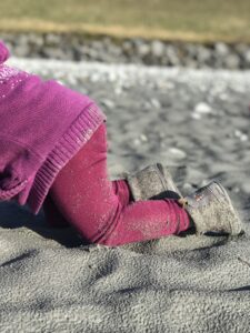 Mädchen krabbelt im Sand mit Barfussschuhen