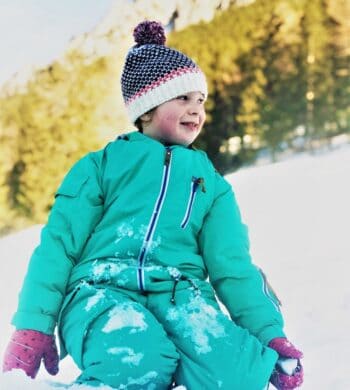 Mädchen kniet im Schnee mit Skianzug